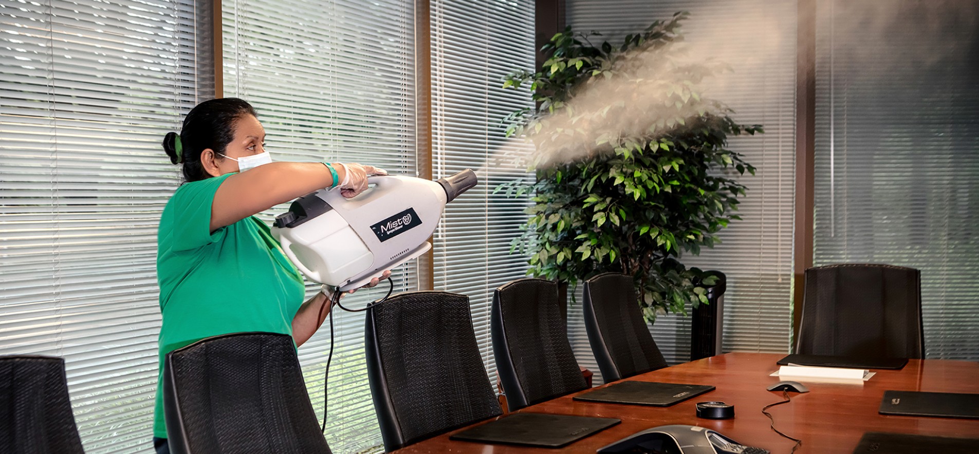 Photo of Level Seven worker in green shirt using a misting machine to spray disinfectant in an office