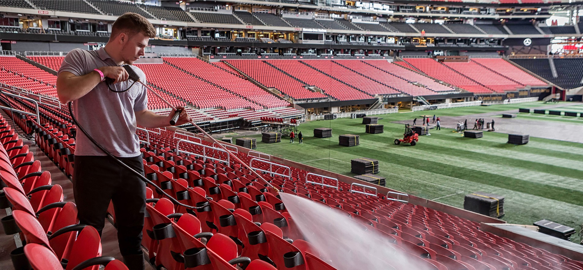 Photo of a Level Seven worker using a pressure washer to clean the seats in a stadium