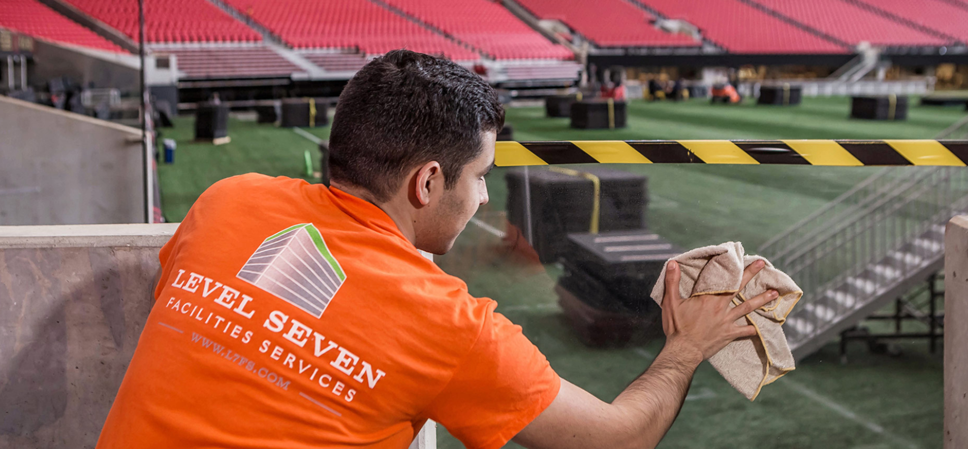 Photo of a Level Seven worker in an orange shirt cleaning a plexiglass panel in a stadium