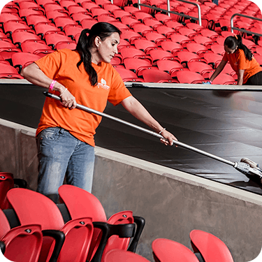 Photo of a Level Seven worker in an orange shirt, cleaning a stadium with other workers visible in the background